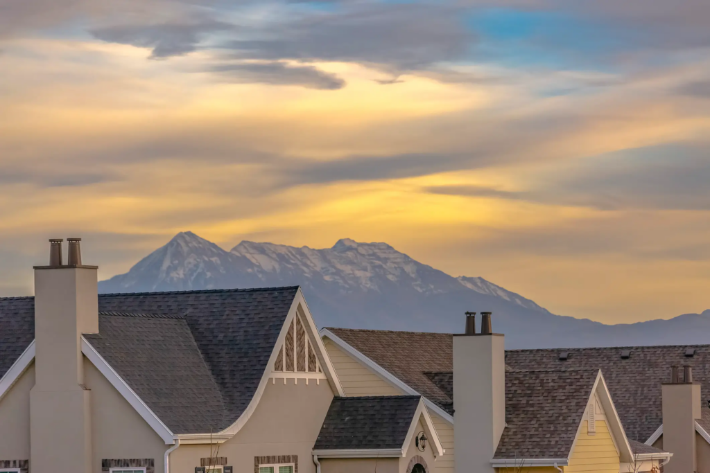 Cache Valley homes with quality roofing against a backdrop of snow-capped mountains and a dramatic winter sky, illustrating the importance of durable roofing during harsh winters.