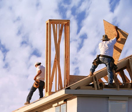 Construction crew installs new plywood sheathing on a commercial roof under clear skies, showcasing Skabelund Roofing’s expert upgrade services for business properties.