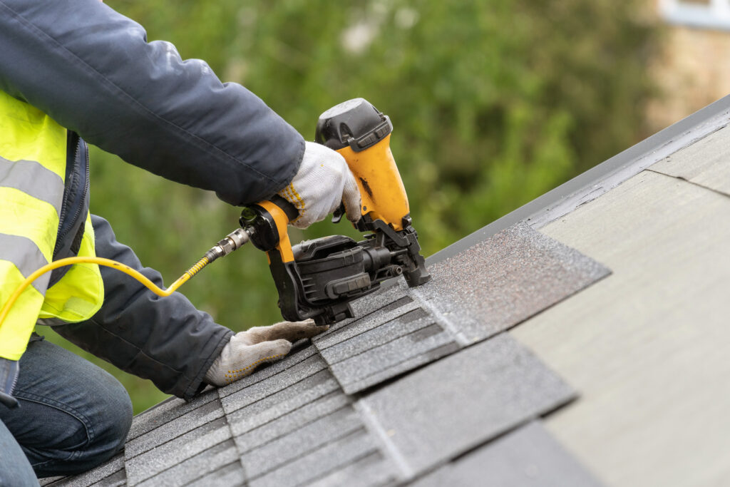 Contractor installing asphalt roof shingles with pneumatic nail gun on residential roof