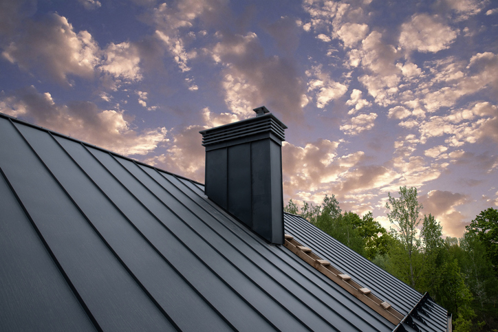 Close-up of a dark grey metal roof with chimney under a cloudy sky
