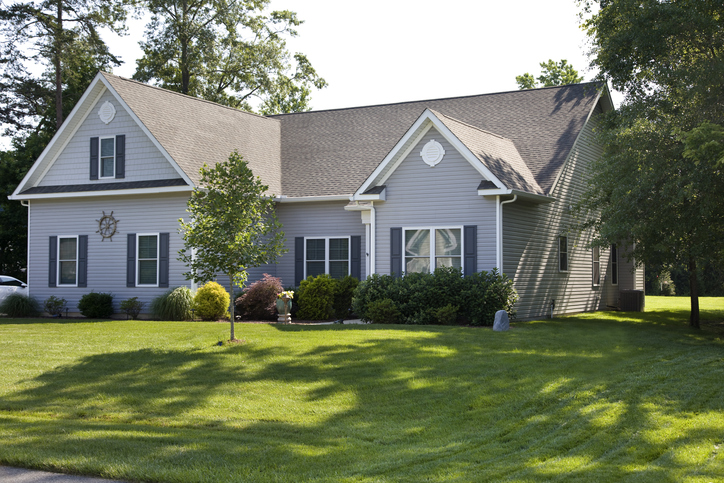 Two-story residential home with a dark gray shingled roof, light gray siding, and well-maintained landscaping, showcasing a high-quality roofing installation.