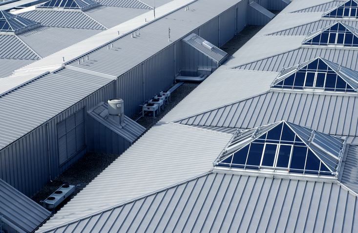 High-angle view of a commercial building with a modern metal roofing system, featuring corrugated panels, skylights, and visible HVAC equipment, showcasing durable and efficient roofing solutions.