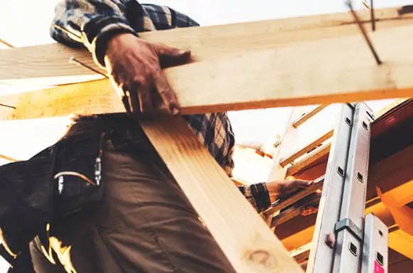 Construction worker carrying wooden beams on a building site in Logan, UT