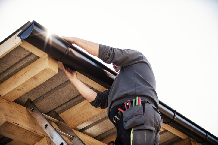 Contractor repairing a black rain gutter on a wooden roof – early signs of gutter damage and repair