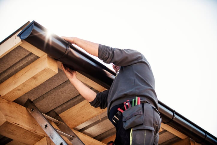 A Contractor repairing a black rain gutter on a wooden roof in Logan, UT